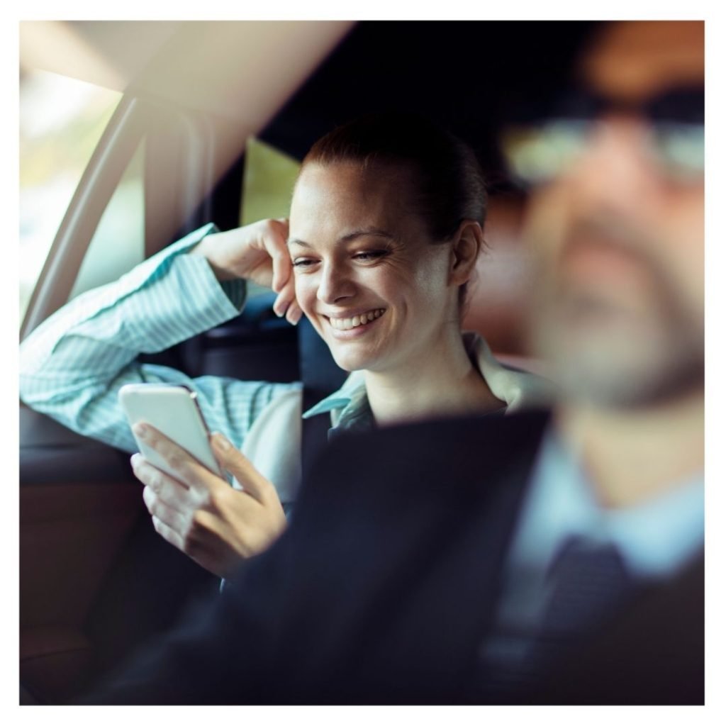 A happy women on her phone in the back of a private transporation