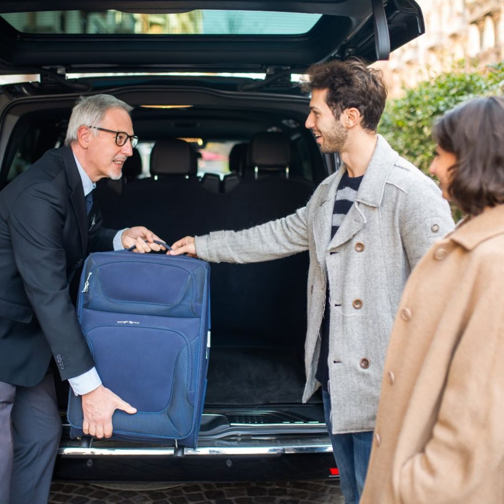 chauffeur helping couple pack luggage in car